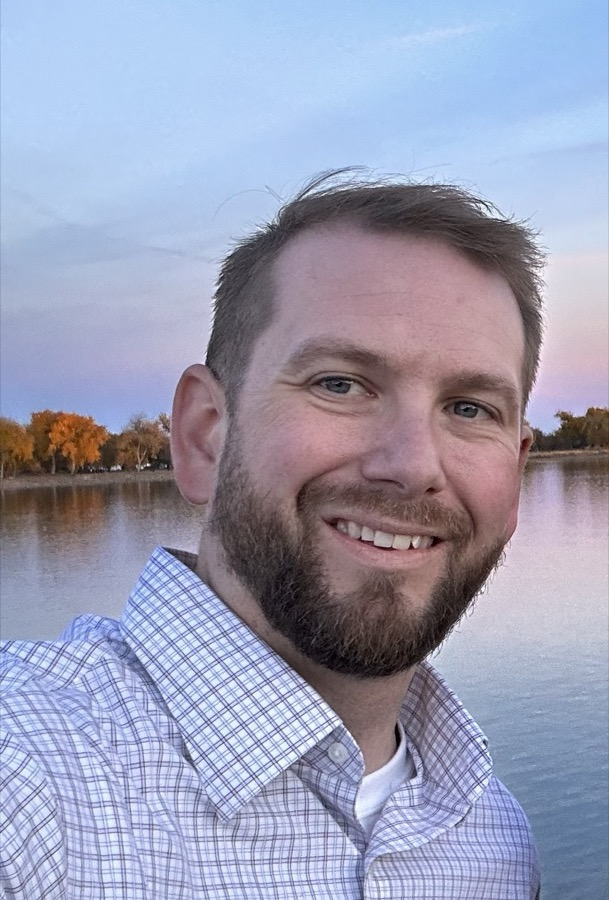 Justin outdoors by a lake at sunset